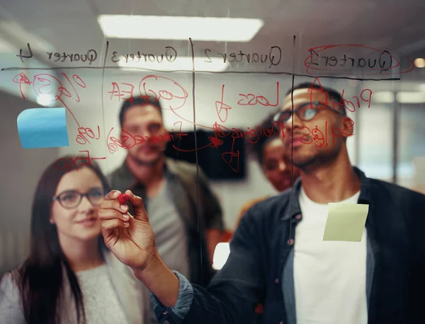 Jóvenes empresarios exitosos escribiendo en tablero de vidrio transparente con marcador rojo en reunión de oficina — Foto de Stock