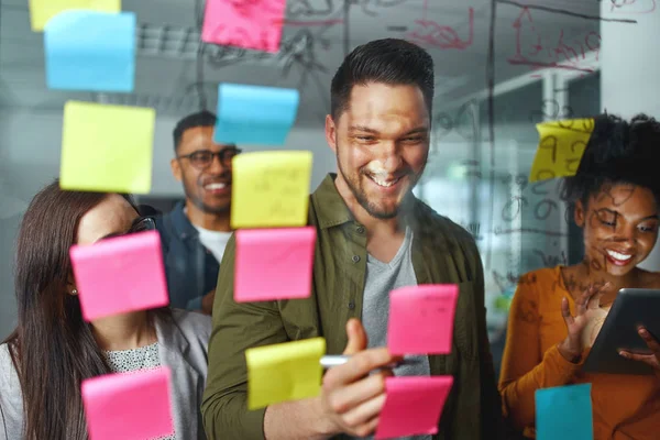 Grupo de pessoas de negócios casuais sorridentes planejando e escrevendo projeto e ideias sobre as notas pegajosas coladas na parede de vidro no escritório moderno — Fotografia de Stock