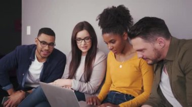 Modern bir ofiste oturan ve bir dizüstü bilgisayara bakan ve takım olarak birlikte çalışan bir grup karışık ırk arkadaşı 