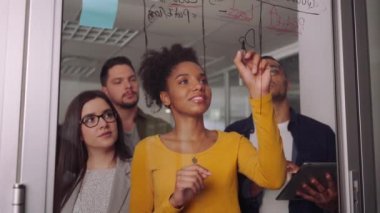 Ofisteki meslektaşına iş kavramını açıklayan cam bir tahtaya yazan afrikalı genç bir iş kadınının portresi