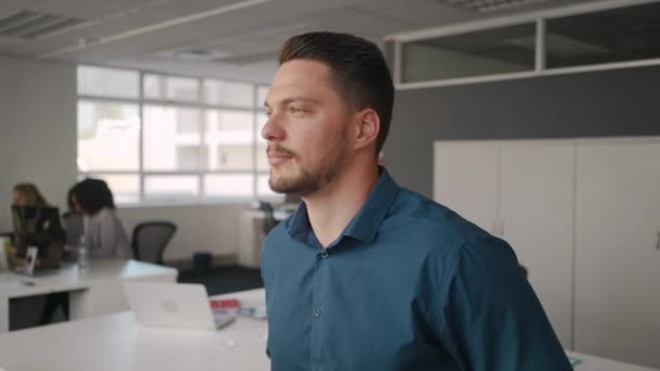 Portrait d'un jeune homme d'affaires confiant et heureux debout dans le bureau souriant et regardant la caméra avec des collègues travaillant en arrière-plan — Video