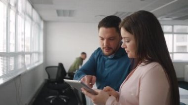 Profesyonel genç işadamı ve iş kadını modern ofiste dijital tablet üzerinde birlikte iş tartışıyor