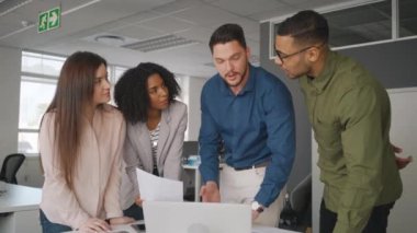 Kendinden emin ekip lideri ve ofiste dizüstü bilgisayarda çevrimiçi projeyi tartışıyor birlikte çalışan çalışanlar