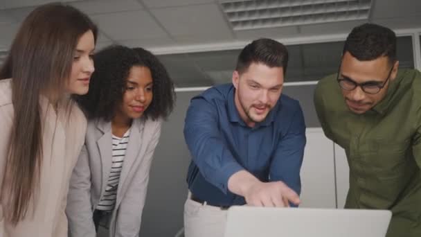 Профессиональный уверенный молодой бизнесмен показывает онлайн-проект и маркетинговую стратегию на ноутбуке своим коллегам в офисе — стоковое видео
