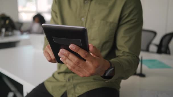 Primer plano de un joven hombre de negocios con camisa sentado en un escritorio blanco usando una tableta digital en la oficina moderna — Vídeo de stock