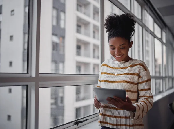 Empresária atraente usando um tablet digital em frente às janelas em um prédio de escritórios com vista para a cidade — Fotografia de Stock