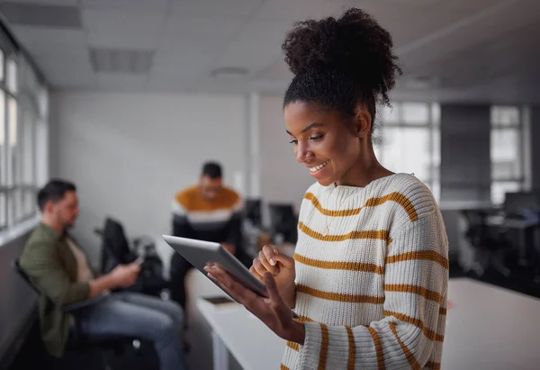 Retrato de una mujer ejecutiva afroamericana vestida casual que sonríe usando tableta digital en la oficina moderna con colegas trabajando en segundo plano — Foto de Stock