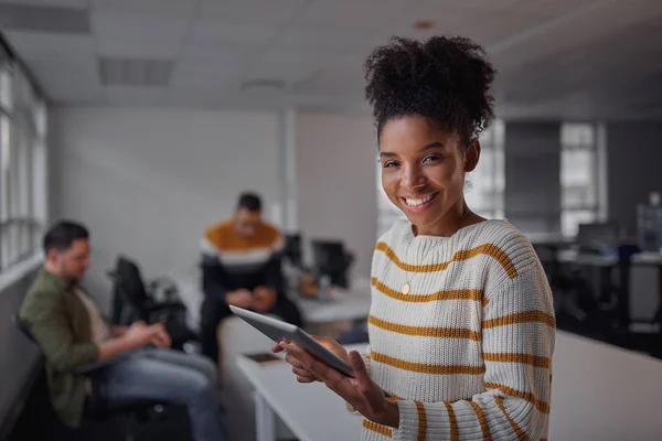 Neşeli genç afro-amerikan iş kadını rahat giyim dijital tablet tutarak gülümseyerek ve arka planda arkadaşları iletişim ederken kameraya bakıyor - kadın girişimci - kadın