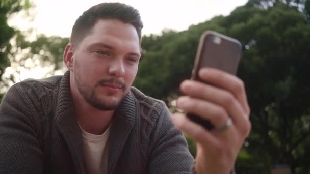 Retrato de joven guapo feliz usando aplicación móvil al aire libre — Vídeos de Stock