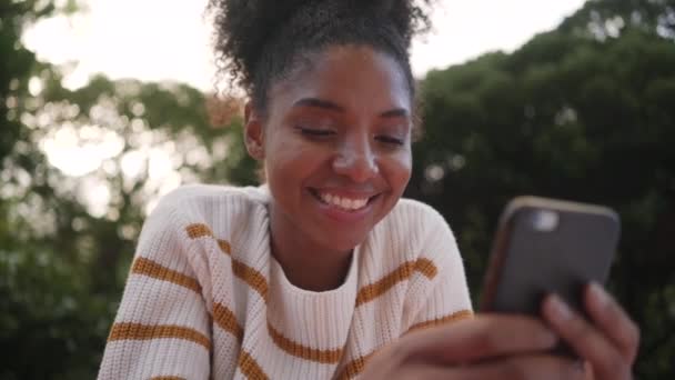 Niski kąt widzenia afrykańskiej młodej kobiety na zewnątrz za pomocą smartfona — Wideo stockowe
