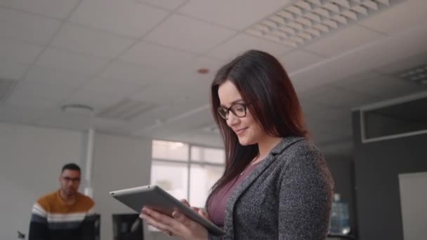 Tilt upp skott av en framgångsrik lycklig ung affärskvinna söka data på digital Tablet och hennes affärsteam pratar med varandra i bakgrunden — Stockvideo