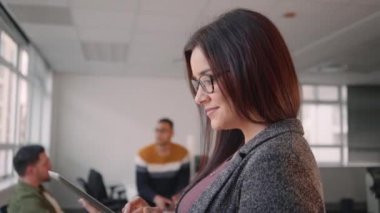 Ofiste arka planda onu iş ekibi ile bilgisayar dizüstü bilgisayar kullanarak kendine güvenen gülümseyen genç iş kadını Portresi