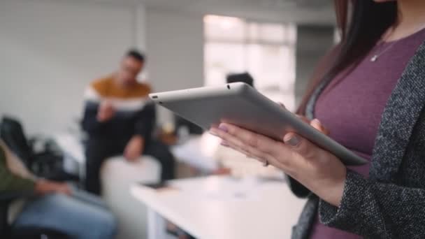 Крупный план предпринимательницы, работающей над цифровым планшетом, пока ее коллеги общаются на заднем плане в офисе — стоковое видео