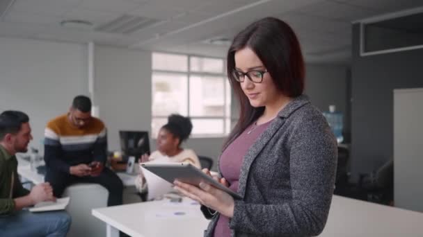 Portrait de heureuse jeune femme d'affaires attrayante en utilisant une tablette numérique avec des collègues vus en arrière-plan — Video