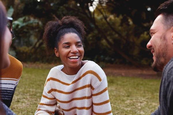 Ritratto di una giovane donna africana sorridente seduta e che si diverte con i suoi amici nel parco — Foto Stock