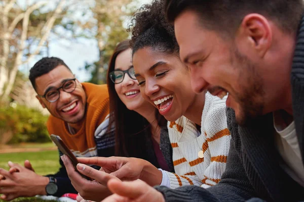 Groupe d'amis multiethniques à l'université couchés ensemble dans le parc profiter de regarder du texte ou de la vidéo sur téléphone mobile - groupe souriant d'étudiants — Photo