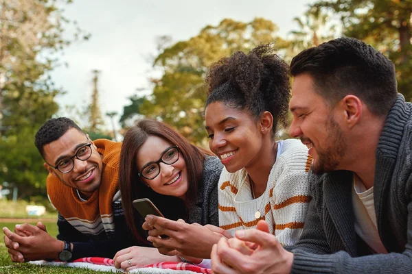 Grupo de felices y diversos amigos mirando a la mujer afroamericana usando su teléfono móvil en el parque en un día de verano - muy feliz grupo joven de amigos — Foto de Stock