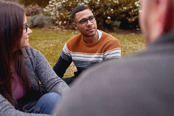 Bonito jovem homem africano sentado junto com amigos multirraciais no parque — Fotografia de Stock