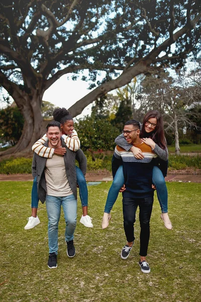 Heureux jeunes hommes portant tour de dos de porc à leurs copines dans un parc souriant - s'amuser à l'extérieur — Photo