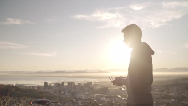 Κινηματογραφικού βίντεο ενός άντρα που βγάζει το κηφήνα του και το κάνει να πετάει πάνω από τα σύννεφα και πάνω από την πόλη σε μια ηλιόλουστη μέρα-φουτουριστική τεχνολογία — Αρχείο Βίντεο