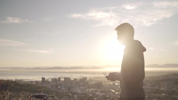 Filmación cinematográfica de un hombre quitando su dron y haciéndolo volar por encima de las nubes y sobre la ciudad en un día soleado tecnología futurista — Vídeo de stock