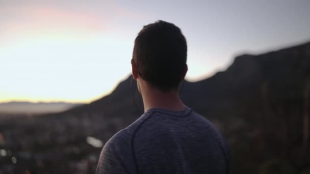 Közeli fel a sportos fiatalember hallgató zene a fülhallgató nézi a városkép kilátás Mountain Top-inspiráció — Stock videók