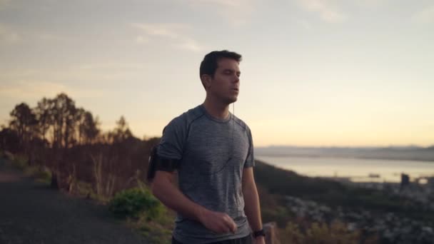 Fitnessläufer läuft auf Berggipfel und hört im Armbindengurt Musik per Handy - Sportler läuft - Stadtbild — Stockvideo