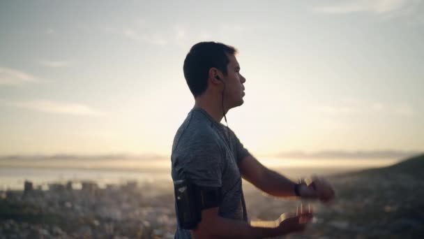 Jonge fitness man runner dragen koptelefoon stretching handen en terug voor het draaien op bergtop bij zonsopgang — Stockvideo