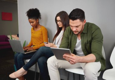 İş görüşmesi öncesinde koridorda ki koltuklarda oturan, akıllı telefon, dijital tablet ve dizüstü bilgisayara göz atan genç iş adayları
