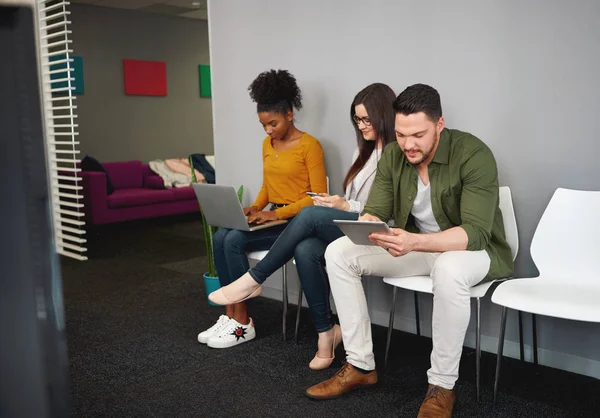 Grupo de jóvenes multiculturales sentados en fila en la silla para la entrevista de trabajo con ordenador portátil, tableta digital y teléfono inteligente — Foto de Stock