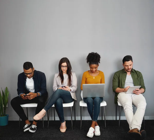 Giovani multietnici seduti in coda e dipendenti dai social media utilizzando smartphone, tablet digitali e laptop nel corridoio dell'ufficio — Foto Stock