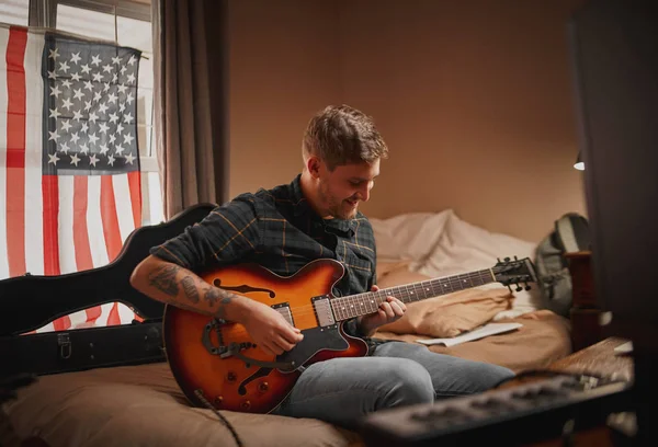 Młody mężczyzna muzyk siedzi na łóżku w sypialni ciesząc się czas gry na gitarze w domu — Zdjęcie stockowe