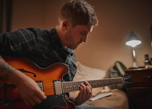 Zbliżenie młodego mężczyzny ćwiczącego grę na gitarze wieczorem w swoim domu — Zdjęcie stockowe