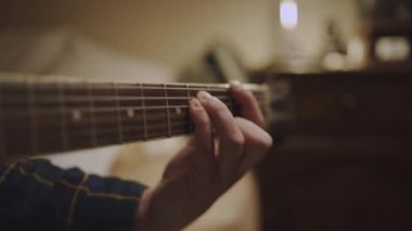 Gitaristin gitar direğinin perdesine yerleştirilmiş gitaristin parmaklarını yukarı kaldır ve akor çal. Gitaristin yakın çekimlerini yap.