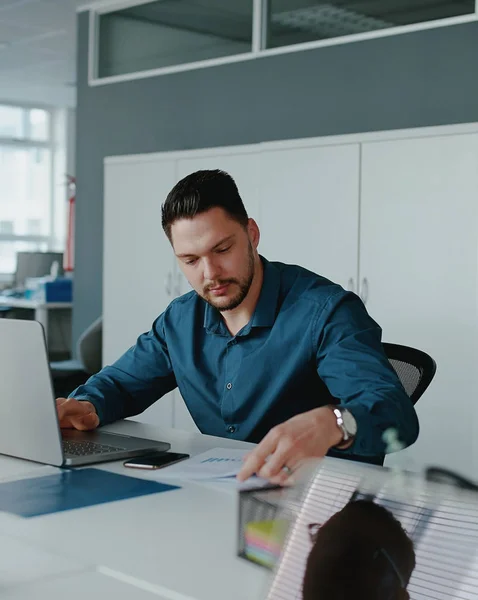 Een jonge mannelijke ondernemer met behulp van laptop computer werken aan rapporten zitten op kantoor — Stockfoto