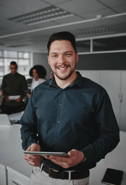 Portret van een succesvolle glimlachende jonge zakenman met digitale tablet in de hand kijkend naar de camera terwijl collega 's een gesprek voeren op de achtergrond in het moderne kantoor — Stockfoto