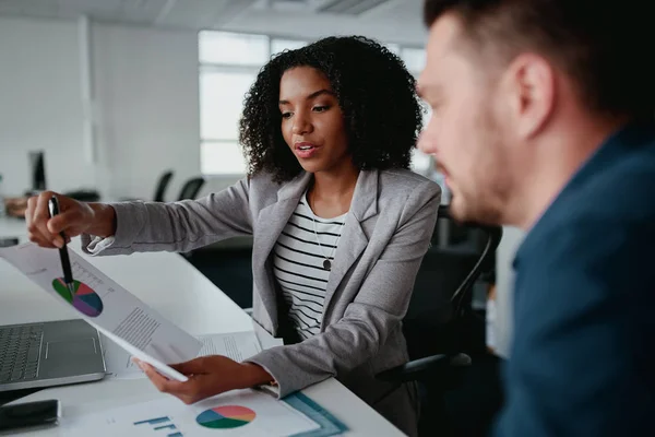 Confident young businesswoman holding document showing increasing statistic to partner in office