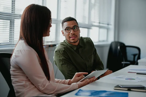 Joven empresaria discutiendo algo positivo usando tableta digital con su colega masculino en el lugar de trabajo —  Fotos de Stock