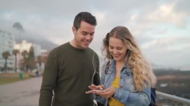 Kulaklıklı mutlu genç arkadaşlar şehir sokaklarında akıllı bir telefondan müzik dinliyorlar.