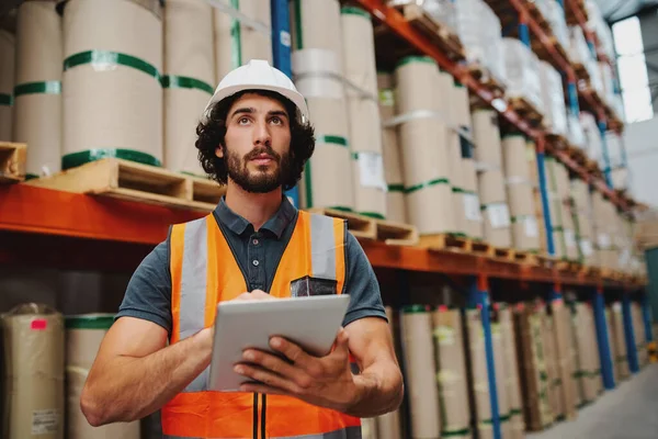 Young caucasian male worker doing stocktaking of product in cardboard box on shelves in warehouse by using digital tablet — Stock Photo, Image