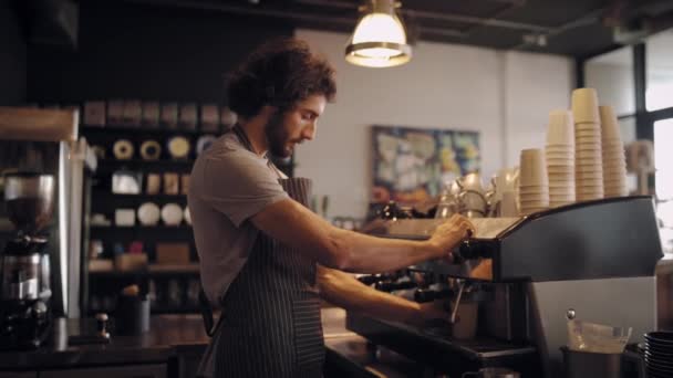 Jonge mannelijke chef-kok in schort het maken van verse koffie in afhaalbeker en geven aan de klant — Stockvideo