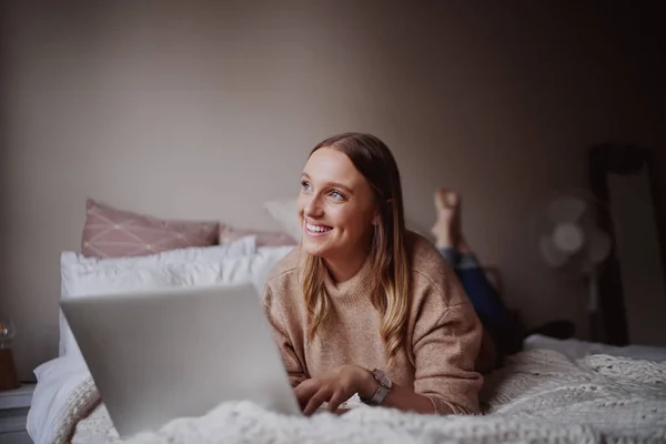 Mooie jonge vrouwelijke ondernemer liggend op haar bed werken aan een laptop in haar huis tijdens lockdown als gevolg van coronavirus - student studeren lezingen online — Stockfoto