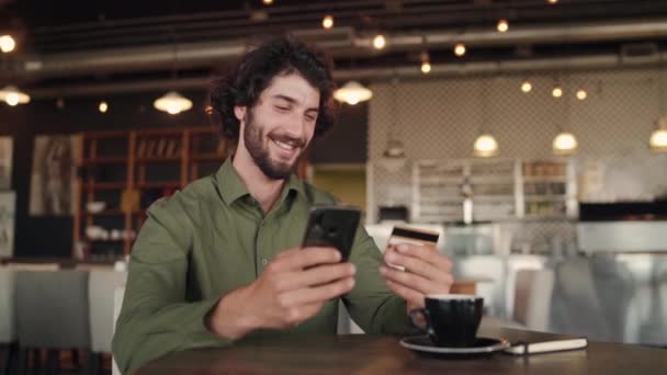 Sorrindo homem caucasiano fazendo compras on-line e compra com cartão bancário enquanto relaxa no café — Vídeo de Stock