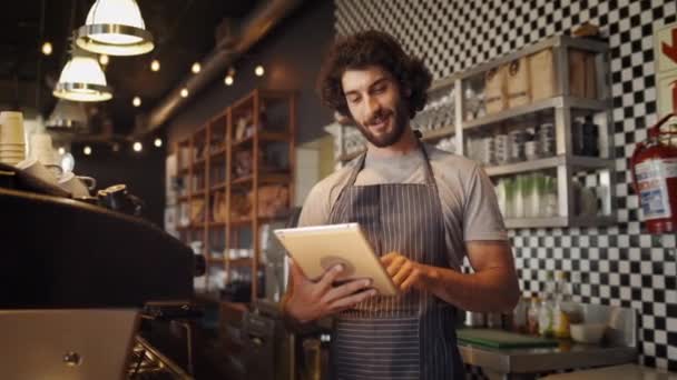 Vrolijke jonge mannelijke cafe eigenaar op zoek naar koffie recepten op internet met behulp van digitale tablet — Stockvideo