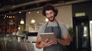 Genç başarılı kafe sahibi internet siparişini kabul ederken siyah çizgili önlük giyerek dijital tablet kullanıyor.