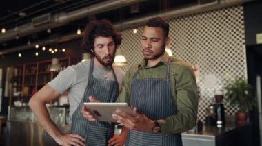 Genç başarılı kafe ortakları dijital tablet kullanarak planı anlarken kafeyi yeniden dekore etmeye çalışıyorlar.