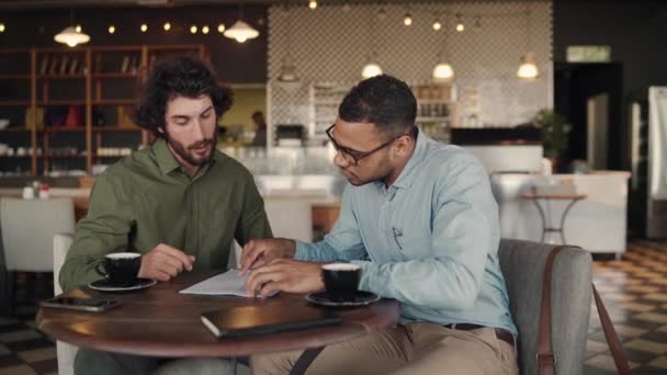 Des partenaires d'affaires caucasiens et africains joyeux signent un contrat avec poignée de main tout en buvant du café dans un café — Video