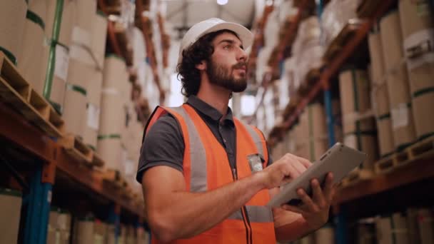 Heureux employé d'entrepôt dans son casque de protection blanc d'une grande usine industrielle vérifie sa tablette à l'intérieur de l'entrepôt de l'entreprise — Video