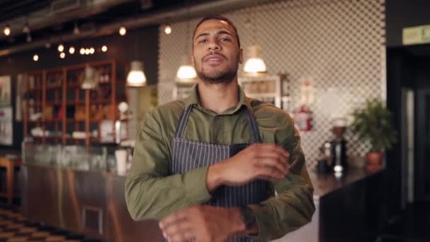 Retrato del exitoso chef africano con delantal negro de pie con los brazos cruzados en la cafetería contra el mostrador — Vídeos de Stock