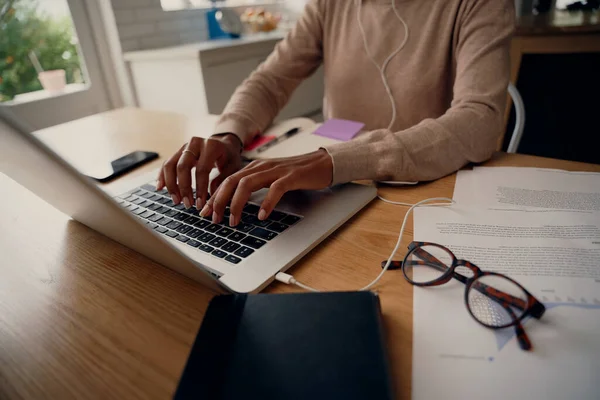 Primer plano de la mano femenina ocupada escribiendo en el teclado mientras está sentada en su casa con documentos y anteojos — Foto de Stock